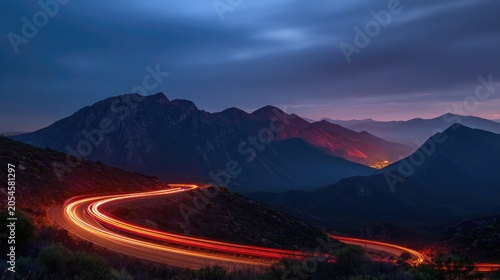 Winding road with light trails at dusk, mountains in background