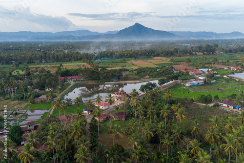Drone aerial view of tropical village, winding river, and volcanic mountain landscape in rural West Sumatra, Indonesia