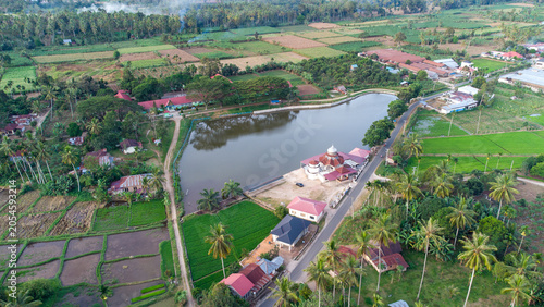 Aerial drone view of a small reservoir and mosque surrounded by lush tropical greenery and rural village in West Sumatra, Indonesia