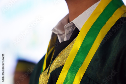 Foto Close-up of a student wearing a green graduation gown with a yellow and green sash during a commencement ceremony, representing education, achievement, and academic success