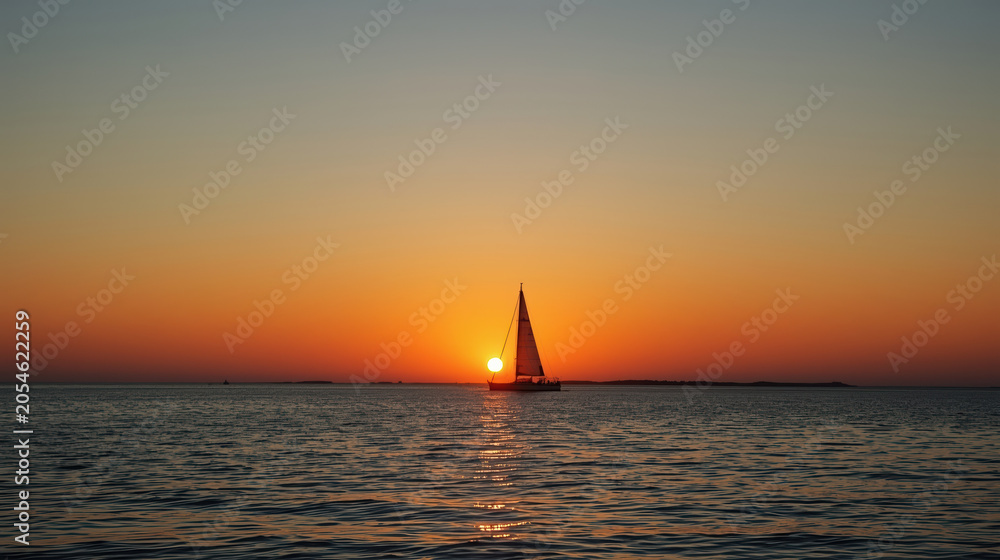 Fototapeta premium Sailboat sunset silhouette on calm sea with warm orange sky