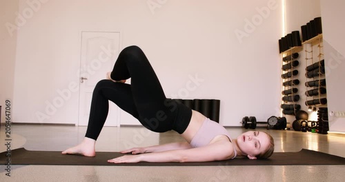 Woman pilates. Core strengthening. Young athlete doing pelvic floor exercise in shoulder bridge yoga pose controlling breath in gym.