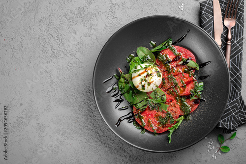 Sliced ripe tomatoes topped with burrata cheese, vibrant green pesto, basil garnish and balsamic reduction on matte black plate