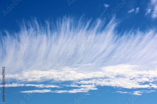 Wispy white cirrus uncinus clouds stretching like paintbrush strokes across a vibrant blue sky