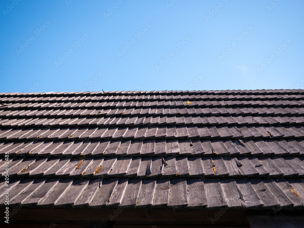 Naklejka premium Traditional wooden shingle roof under a clear blue sky, showcasing natural roofing materials, rustic architecture and durable construction with ample copy space.