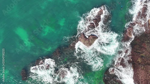 Drone video aerial view of waves crashing onto rocks near a beach in Sydney in Summer 