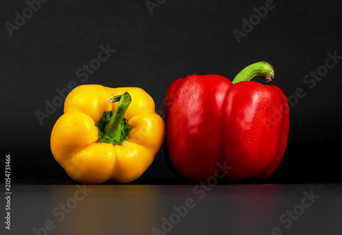 Yellow and red sweet bell peppers side by side on black
