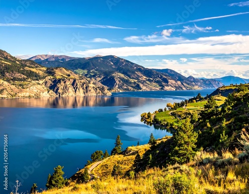 Scenic Mountain Lake Reflecting Blue Sky Along Sunny Hillside Landscape