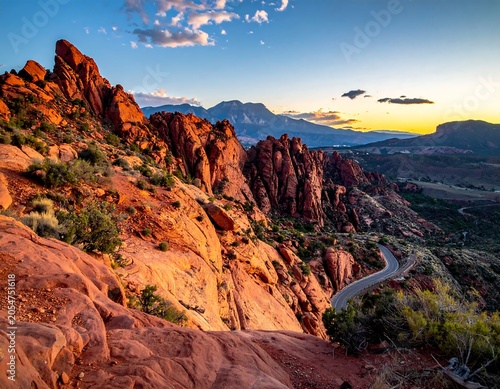 Vibrant Red Sandstone Cliffs Overlooking Winding Road at Sunset in Desert Mountain Landscape