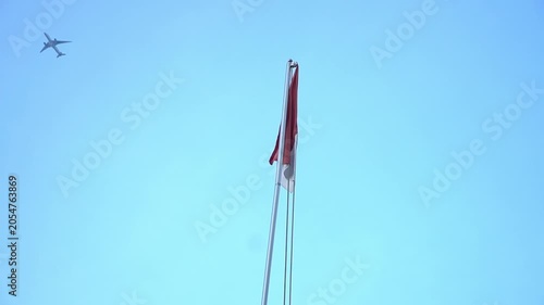 Small airplane flying through clear blue sky past national flag