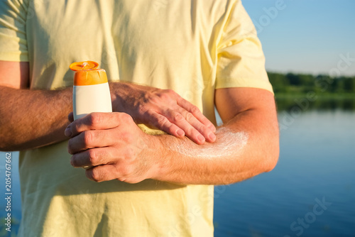 Obraz na plátně Man applies SPF sunscreen to arm in sunny outdoor setting near water