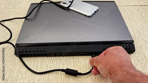 Person disconnects laptop charger from rear port, highlighting power supply, device care, workspace setup, and everyday computing tasks in a modern technology environment