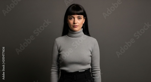 Professional portrait of a young woman with bangs wearing a gray turtleneck sweater against a dark gray studio background