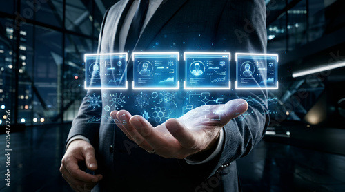 Businessman holding holographic interface showing four candidate profiles with analytical data charts and graphs in a modern corporate office at night for recruitment purposes.