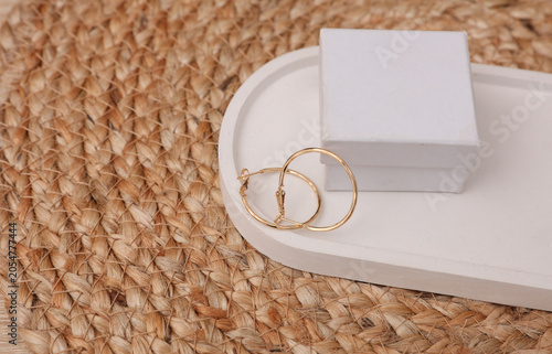 Gold earrings with box in a plaster tray on a woven straw mat. Jewelry product presentation