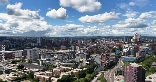 Panoramic aerial view across Leeds city centre featuring the Leeds and Liverpool Canal modern skyline residential developments commercial buildings and urban regeneration under dramatic summer clouds