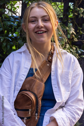 Fotografie Woman early 20s smiling and standing in garden wearing white shirt and brown cro