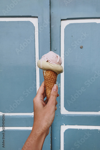Summer Bliss: Close-Up of a Hand Holding a Flavorful Ice Cream Cone Against a Bright Blue Wall