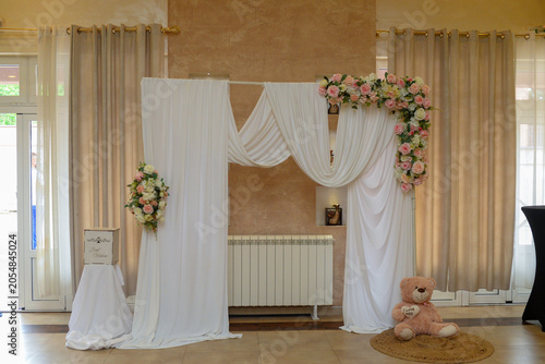 Decoration as a background for photos with the newlyweds. A white curtain, bouquets of roses, a teddy bear holding a heart with the words 