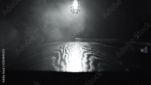 Mysterious workspace with a single light source illuminating a wooden table and smoke-filled atmosphere