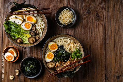 Traditional ramen with jerked pork or chicken.  With udon or ramen noodles. Served in classic bowls. Gyoza dumplings and mushrooms in the background.
