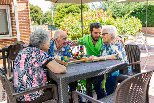 Fotografie Caregiver assisting three elderly people playing with a bead maze toy during an