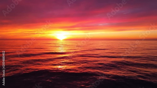 Dramatic sunset over calm ocean water, vibrant orange and pink sky reflecting on the shimmering sea surface, serene natural landscape