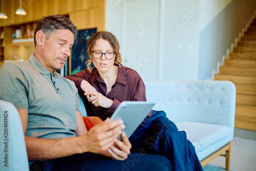 фотографія Man and woman relaxing at home, looking at a digital tablet screen together and