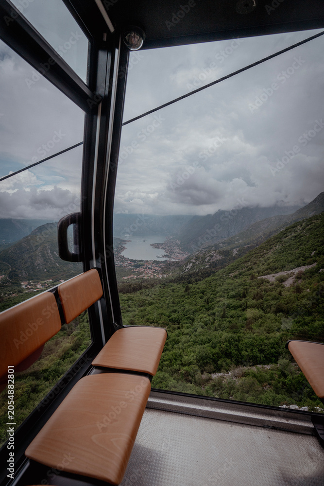 Fototapeta premium Inside view of a cable car cabin with a breathtaking panoramic outlook of mountains, sea bay, and clouds.
