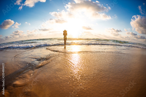 Slim woman on the beach with beautiful sea sunset in the background. Happy young woman feeling free and cheerful while walking barefoot on the beach at sunset during summer holidays.
