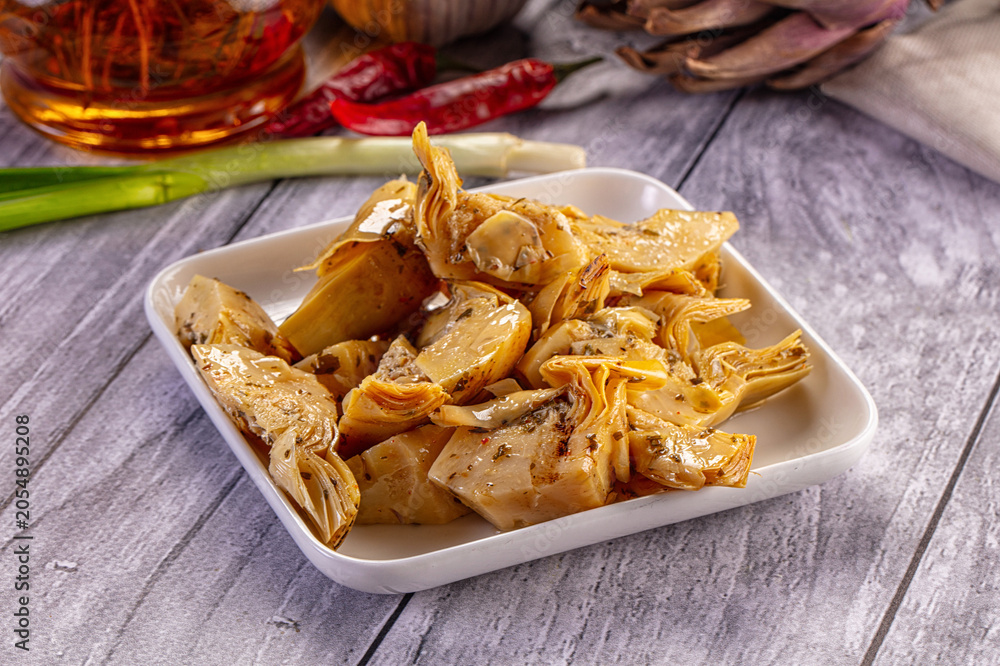 Fototapeta premium Marinated artichoke hearts with herbs and chili peppers on white plate