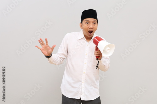 Konstfotografi Asian Muslim man announces something by shouting sideways using a megaphone, standing alone on a gray background