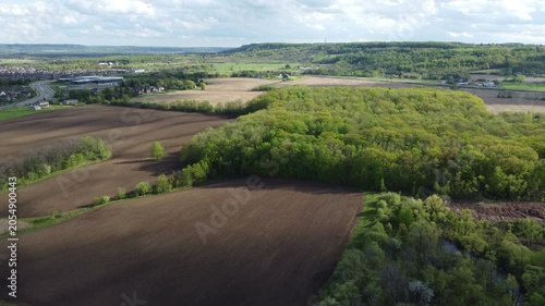Aerial view of Milton, Ontario, Canada as shot from a drone on a mixed sunshine and clouds spring day in May, 2022. Flying southwest towards Bronte and the Escarpment over fields and trees.