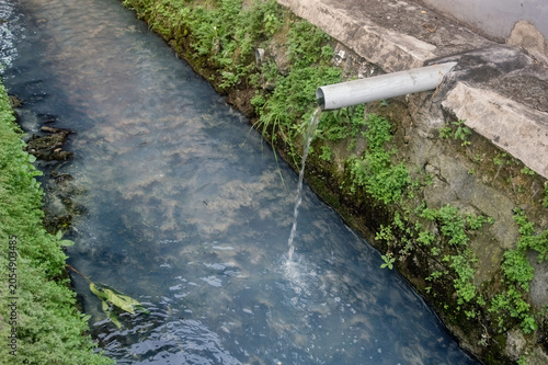 Cuadro en lienzo Wastewater flowing from PVC drainage pipe into open concrete sewer ditch system