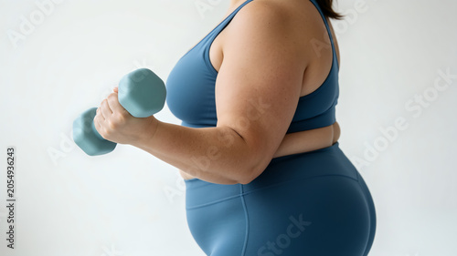 Side view of plus size woman in sportswear training with dumbbell. Body positivity, fitness, and weight loss concept.