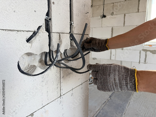 electrical wiring in a new building. A male electrician installs an electrical cable into the wall of a new building. Construction and repair