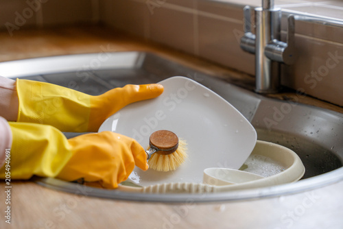 Принти на полотні Cleaning dishes in a kitchen sink with yellow gloves and a brush during the day
