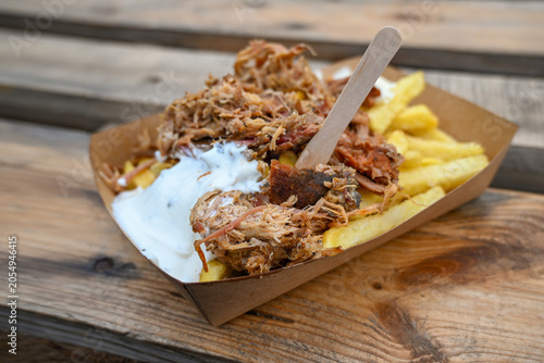 Street food, pulled pork with French fries and sour cream served in a paper bowl on rustic wooden planks, selected focus