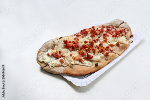 Rustic bread topped with sour cream, onions and bacon, baked in the oven, in Germany called Swabian Pizza or Dinnete, street food on a white table, copy space, selected focus