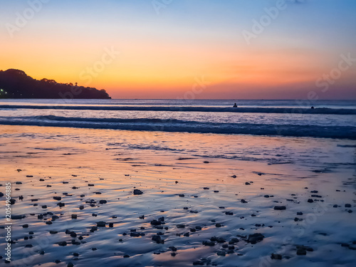 Fotografie Jimbaran Beach shoreline at twilight with orange afterglow sky and silhouetted h