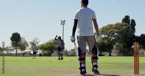 Diverse group running and bowling on grassy field batsman hitting ball to score runs