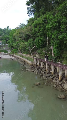 aerial drone pull away shot of a young romantic couple walking at a tropical beach resort with overwater bungalow. Luxury overwater villas on blue lagoon in Weh island, Sabang Aceh, Indonesia