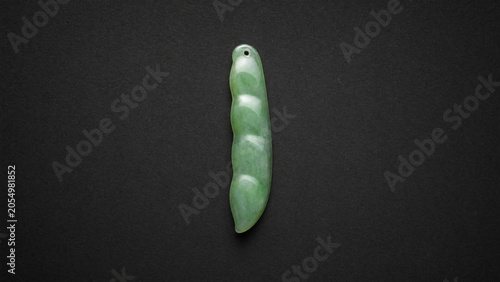 A slender green jade pendant shaped like a silique on a dark background