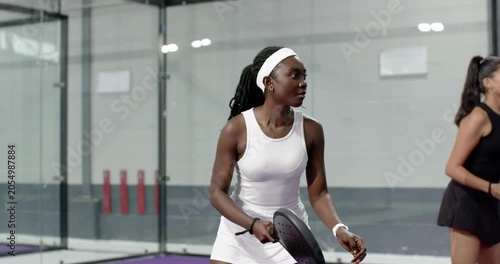 female friends lunging and swinging paddles on purple padel court following opponent shot