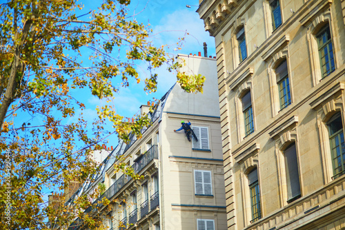 Rope access worker cleaning or maintaining a residential building facade in Paris, France