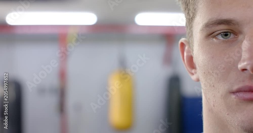 Male athlete spotting yellow punching bag at boxing gym shifting muscles and forming smile