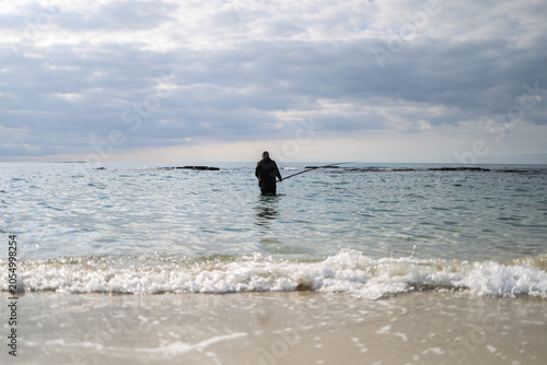 Lone Fisherman Standing in Shallow Ocean Waters Casting a Fishing Line Under a Soft Cloudy Sky