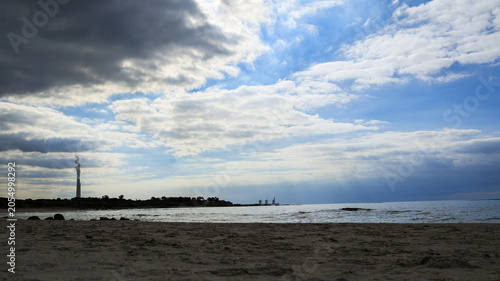 Dramatic Seascape with Contrast Between Stormy Clouds and Sunlight Over a Coastal Industrial Chimney Landscape