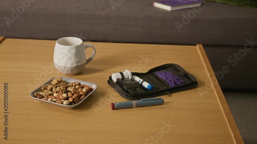 Close up on diabetes testing kit, insulin pen, and plate of mixed nuts sitting on wooden table. Clip ideal for healthcare marketing, diabetes awareness, and chronic disease management campaigns