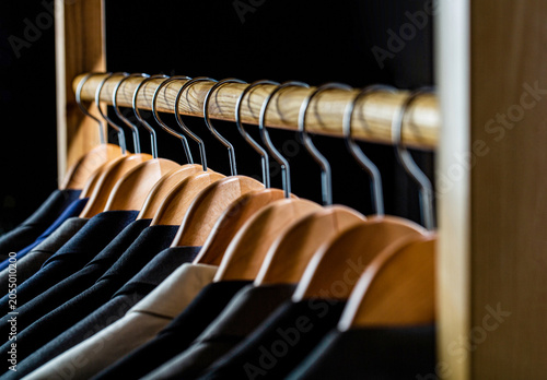 Men suits in different colors hanging on hanger in a retail clothes store, close-up. Mens shirts, suit hanging on rack. Hangers with jackets on them in boutique. Suits for men hanging on the rack